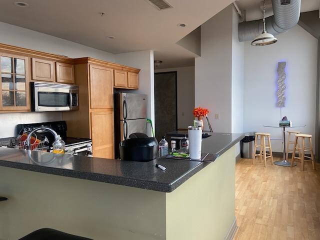 kitchen featuring visible vents, light wood-style flooring, dark countertops, stainless steel appliances, and glass insert cabinets