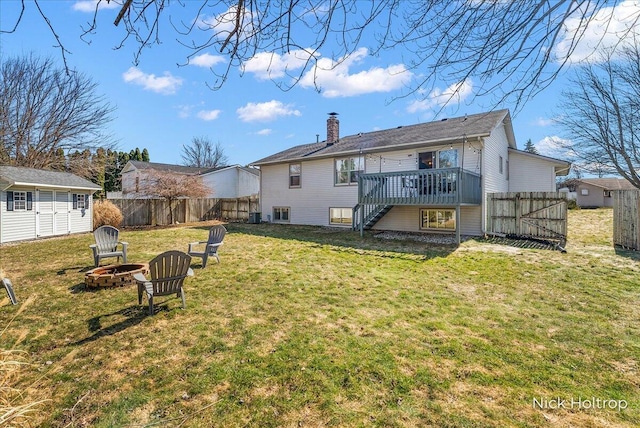 back of property with stairway, fence, a wooden deck, a chimney, and a fire pit