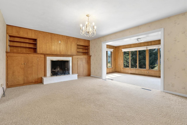 unfurnished living room with carpet, a chandelier, a high end fireplace, and wallpapered walls