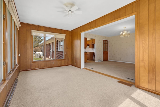 empty room featuring visible vents, baseboards, carpet floors, baseboard heating, and ceiling fan with notable chandelier