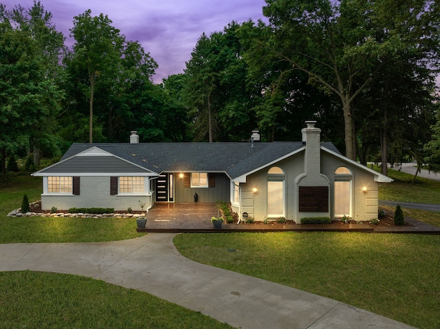 single story home featuring a front yard, driveway, brick siding, a chimney, and board and batten siding