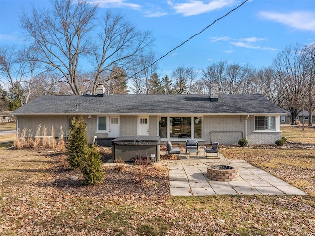 back of house featuring a patio, an outdoor fire pit, brick siding, a chimney, and a hot tub