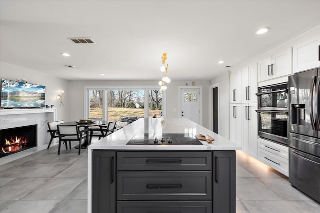 kitchen with a high end fireplace, visible vents, black electric stovetop, white cabinets, and stainless steel fridge