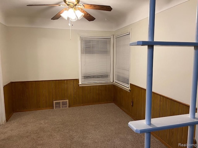 spare room with visible vents, a wainscoted wall, carpet floors, wood walls, and ceiling fan