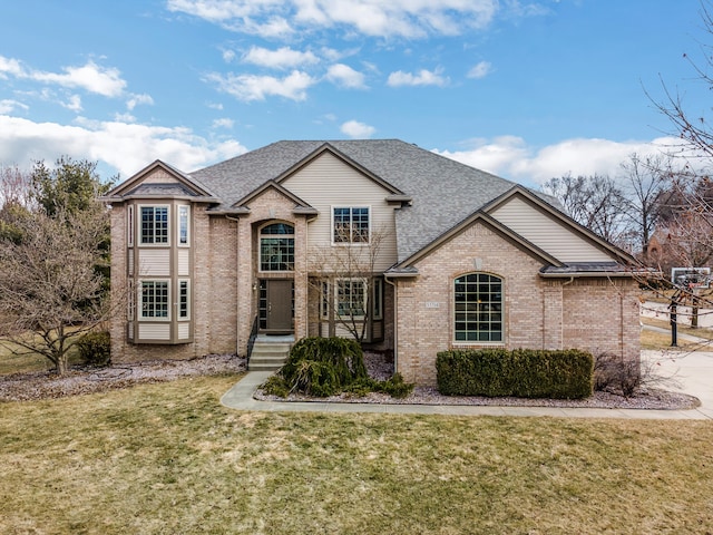 french country style house featuring a front lawn, brick siding, and roof with shingles