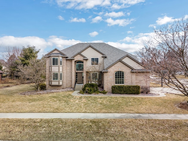 french country home featuring brick siding, a front yard, and a shingled roof