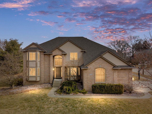 view of front of home featuring brick siding, a front lawn, and roof with shingles