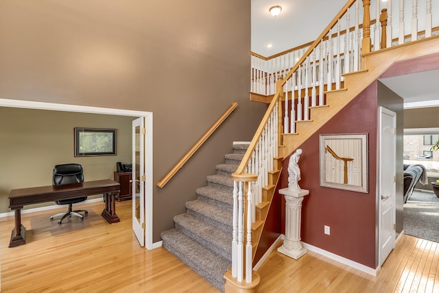 stairway with hardwood / wood-style flooring, baseboards, and a towering ceiling