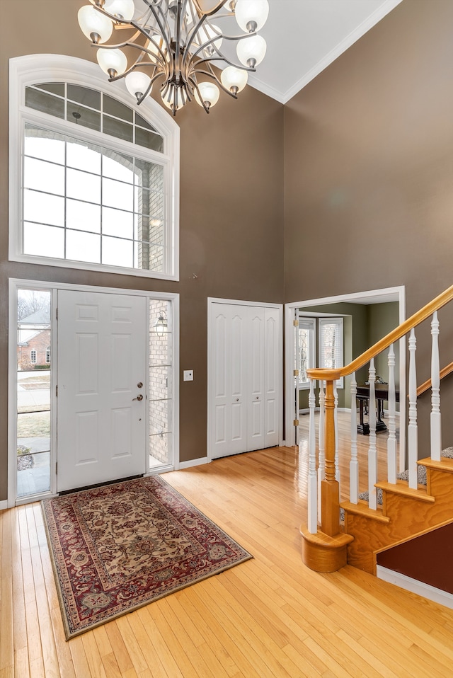 entryway with ornamental molding, hardwood / wood-style flooring, a towering ceiling, stairway, and a chandelier