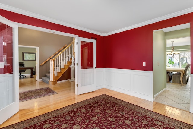 empty room featuring ornamental molding, wood finished floors, wainscoting, a chandelier, and stairs