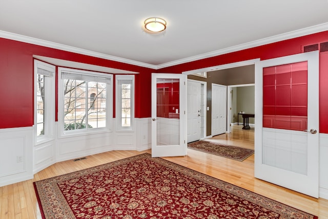 entrance foyer featuring a wainscoted wall, hardwood / wood-style flooring, visible vents, and ornamental molding