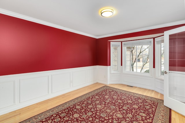 unfurnished room with ornamental molding, wood finished floors, visible vents, and wainscoting