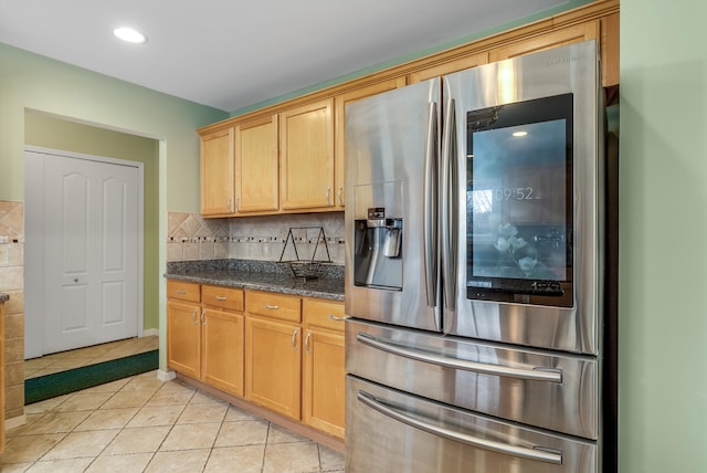 kitchen with dark stone countertops, light tile patterned floors, recessed lighting, stainless steel refrigerator with ice dispenser, and backsplash