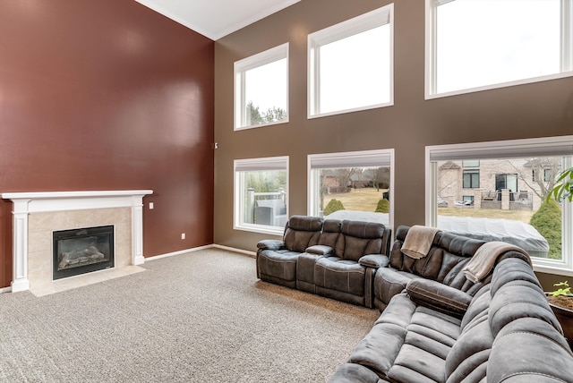 carpeted living room featuring a towering ceiling, baseboards, ornamental molding, and a tiled fireplace