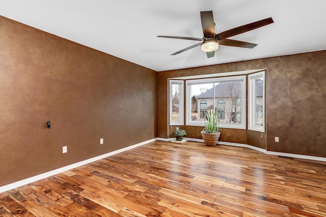 empty room featuring ceiling fan, visible vents, baseboards, and wood finished floors