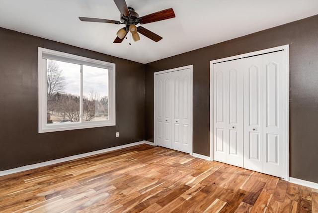 unfurnished bedroom with a ceiling fan, baseboards, light wood-type flooring, and multiple closets