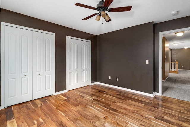 unfurnished bedroom with wood finished floors, baseboards, two closets, and ceiling fan