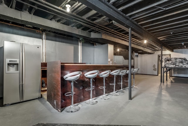 unfinished basement featuring a bar and stainless steel fridge with ice dispenser