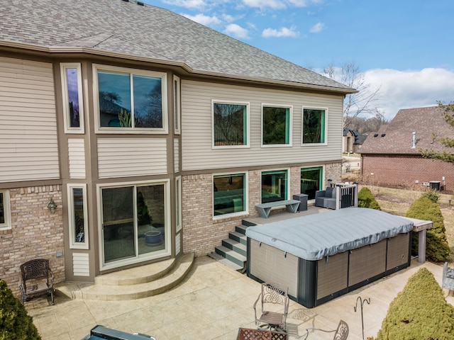 rear view of house featuring a patio, brick siding, and roof with shingles