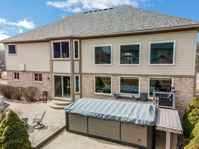 back of property featuring brick siding, a shingled roof, and a patio