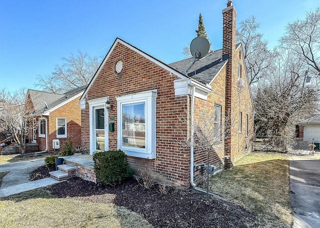 view of property exterior featuring brick siding, roof with shingles, a chimney, and fence