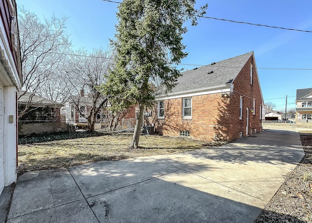 back of property with brick siding, a shingled roof, driveway, and fence