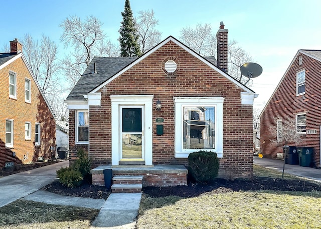 bungalow featuring brick siding, roof with shingles, and a chimney