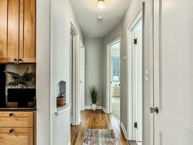 hallway featuring light wood finished floors and baseboards