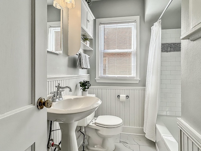 bathroom with toilet, marble finish floor, shower / tub combo with curtain, and wainscoting