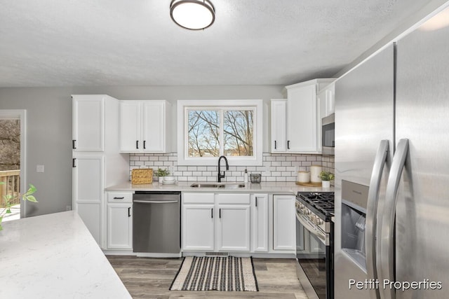 kitchen with light wood finished floors, a sink, stainless steel appliances, white cabinets, and tasteful backsplash