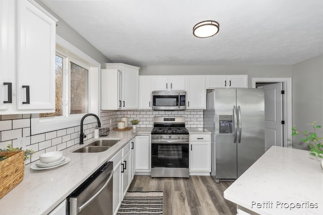 kitchen with light stone counters, light wood-style flooring, appliances with stainless steel finishes, white cabinetry, and a sink