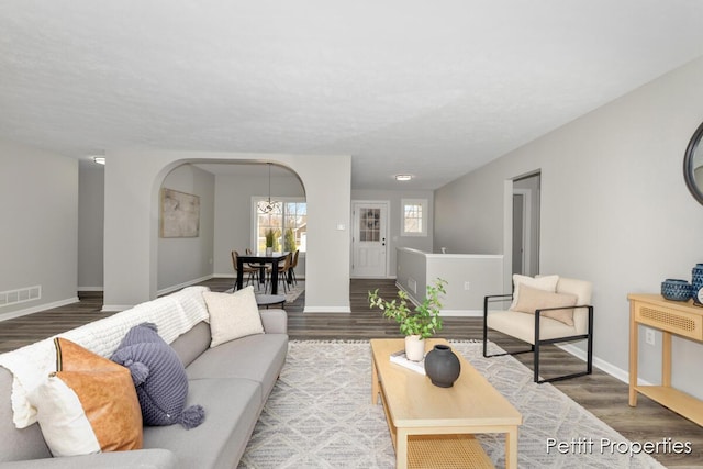 living room featuring visible vents, baseboards, arched walkways, and wood finished floors