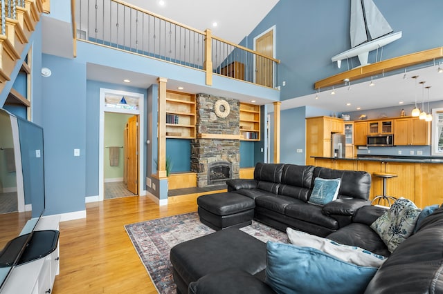 living room featuring a stone fireplace, a high ceiling, light wood-type flooring, and baseboards