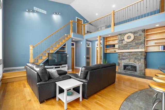 living room with visible vents, stairs, a fireplace, wood finished floors, and high vaulted ceiling