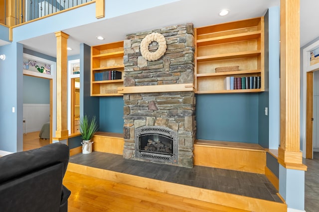 living room featuring built in shelves, wood finished floors, decorative columns, a fireplace, and recessed lighting