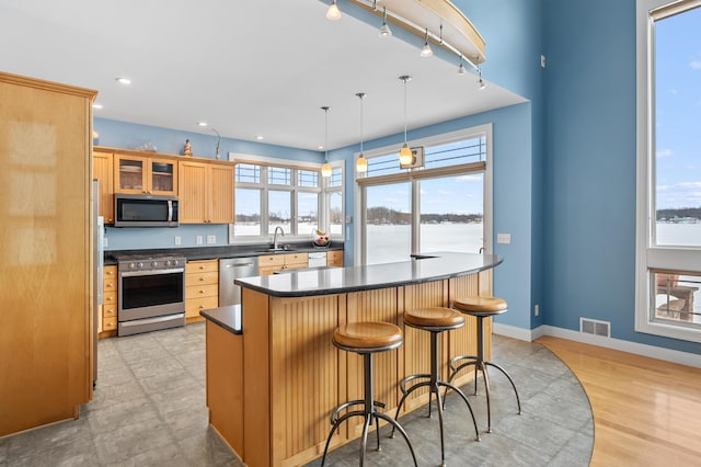 kitchen featuring visible vents, a sink, dark countertops, stainless steel appliances, and glass insert cabinets