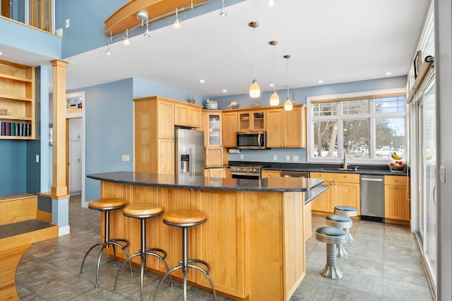 kitchen with glass insert cabinets, a breakfast bar area, decorative columns, stainless steel appliances, and a sink