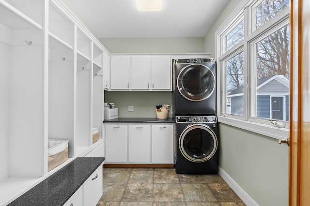 washroom with stone finish flooring, cabinet space, stacked washer and dryer, and baseboards