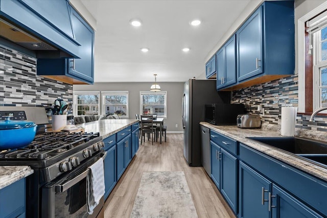 kitchen featuring light wood finished floors, premium range hood, stainless steel appliances, blue cabinets, and a sink