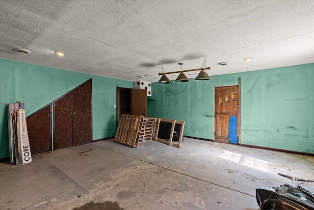 miscellaneous room with a textured ceiling, concrete flooring, and baseboards