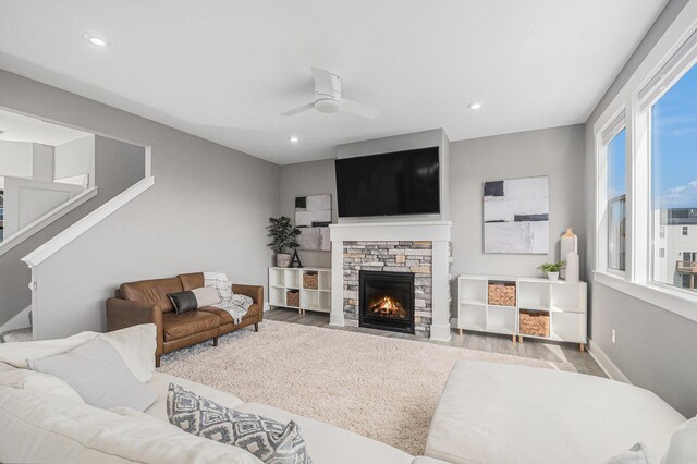 living room with a ceiling fan, wood finished floors, recessed lighting, a stone fireplace, and baseboards