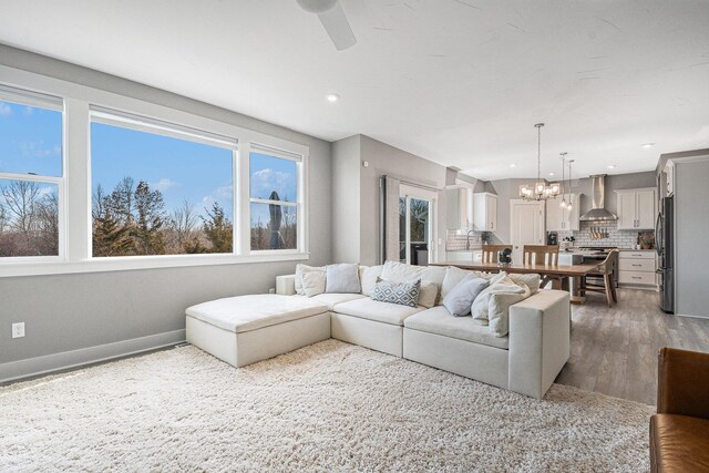 living area with recessed lighting, ceiling fan with notable chandelier, baseboards, and wood finished floors