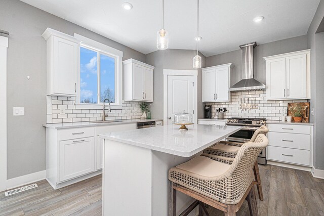 kitchen with visible vents, a center island, wall chimney range hood, stainless steel range, and a sink