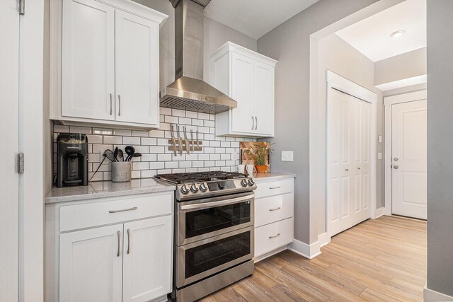 kitchen featuring white cabinetry, light wood-style floors, wall chimney range hood, and range with two ovens