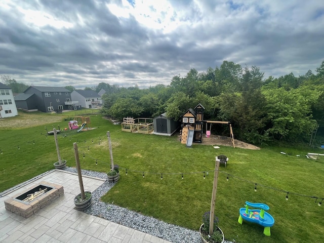 view of yard featuring an outbuilding, a playground, an outdoor fire pit, a storage shed, and a patio area