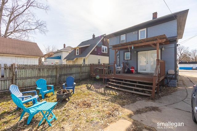 back of property featuring a deck, fence, french doors, a fire pit, and a chimney