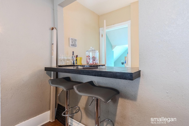 bar featuring a bar, a textured wall, and baseboards