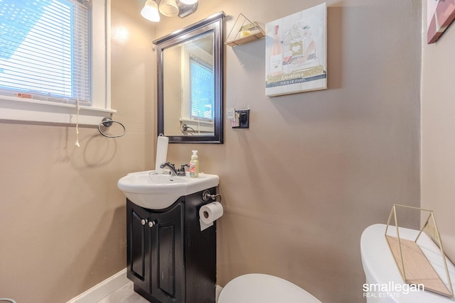 half bathroom featuring a healthy amount of sunlight, toilet, vanity, and baseboards