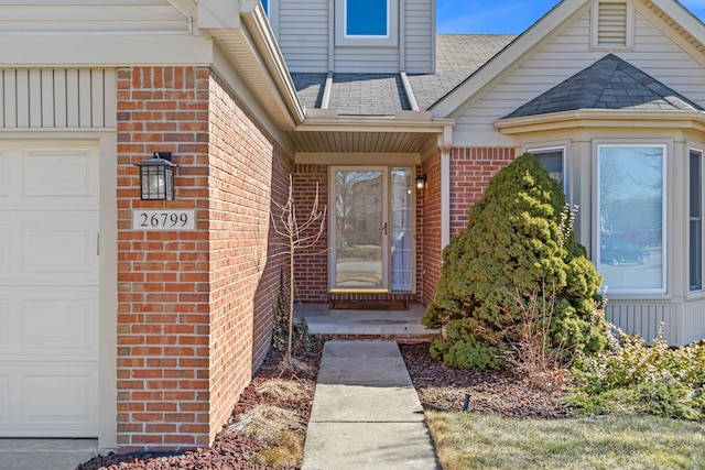 property entrance with brick siding, an attached garage, and a shingled roof