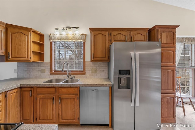 kitchen with a sink, stainless steel appliances, brown cabinetry, and vaulted ceiling